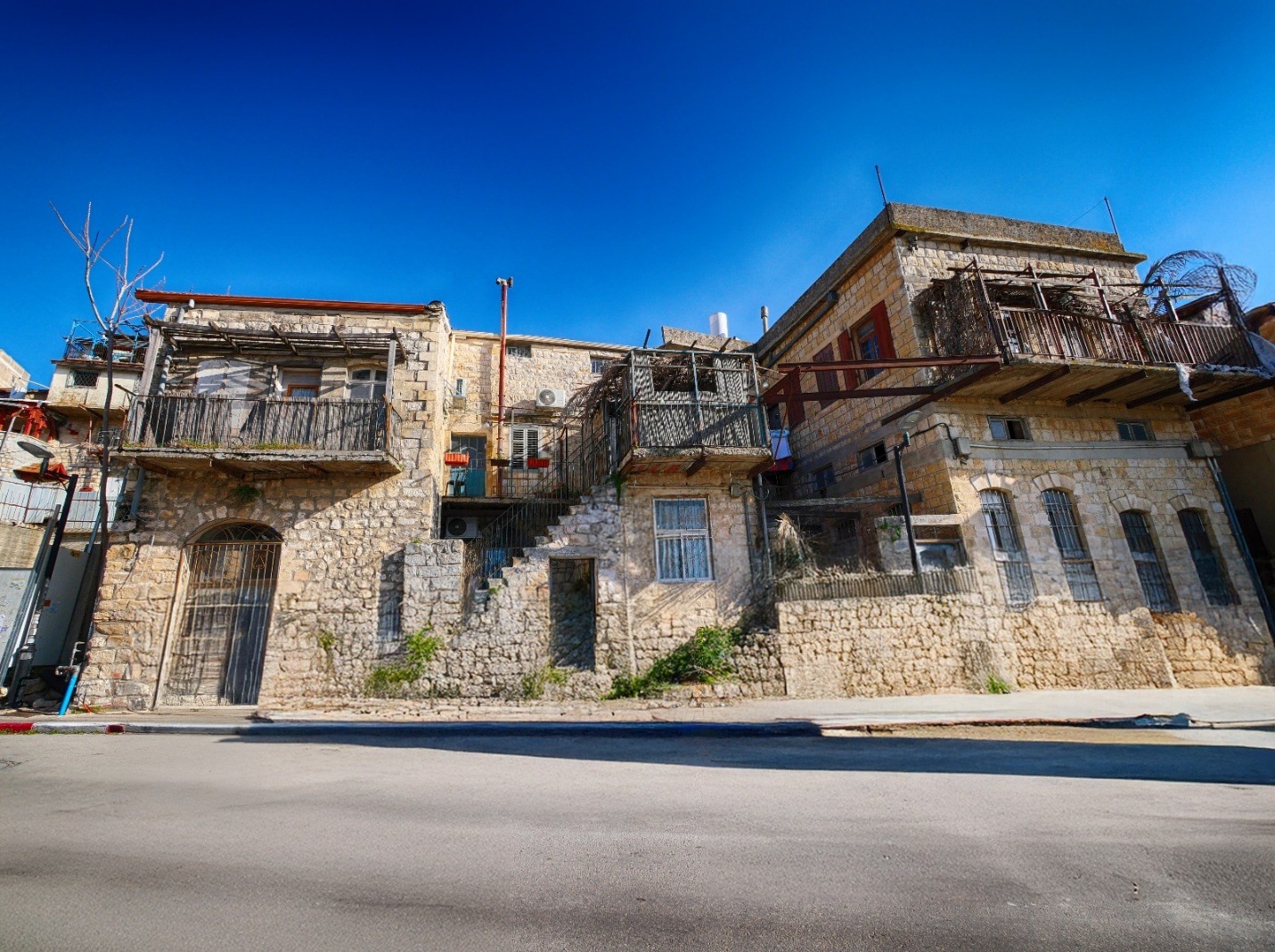Historic stone buildings with balconies and metal railings, situated along a street